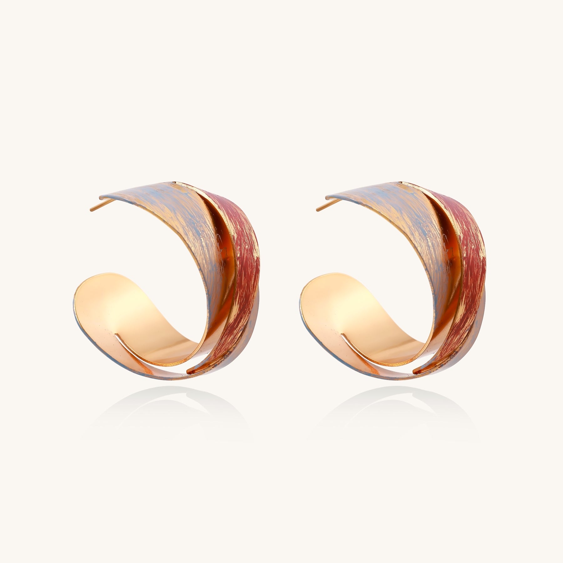 Twisted gold-plated brass earrings with multicolored enamel brushstroke patterns in burgundy and blue on white background.