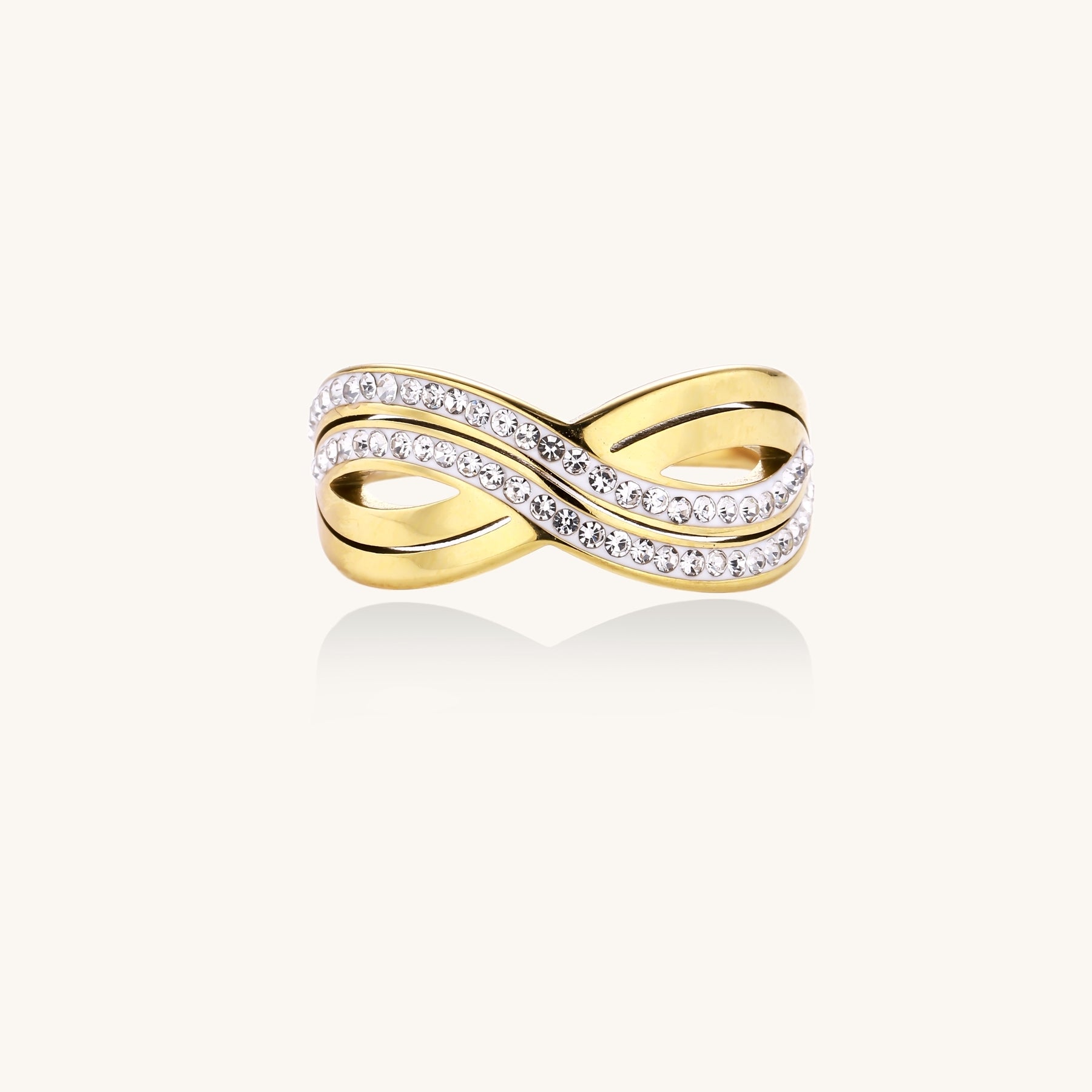 Gold-plated stainless steel ring with crossed infinity bands adorned with sparkling rhinestones against cream background.
