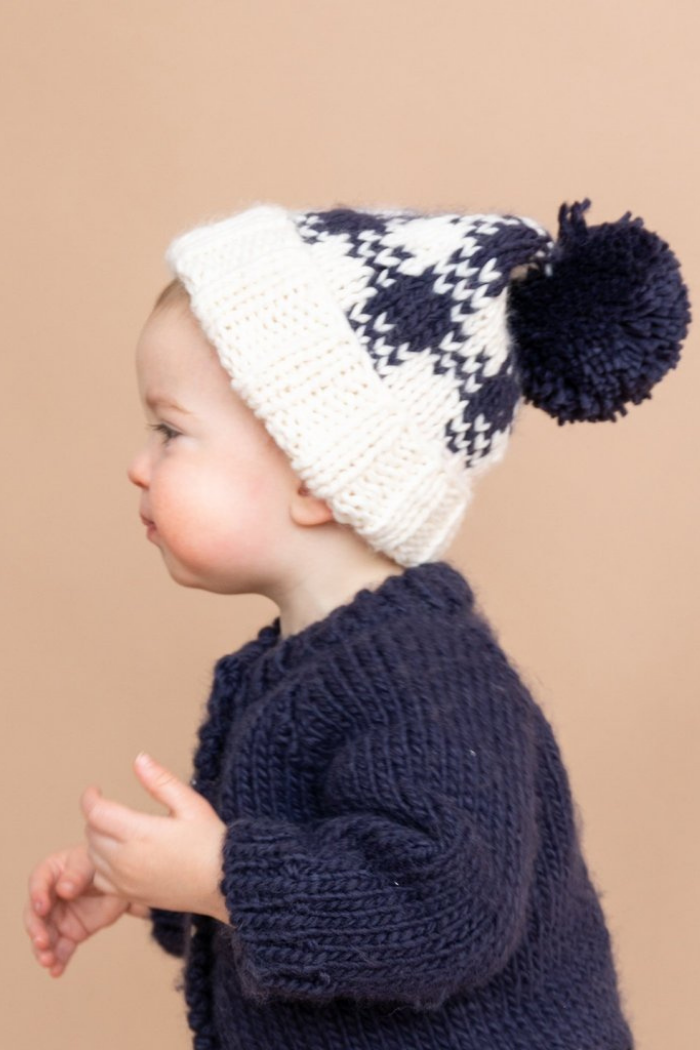 Baby boy wearing Blueberry Hill buffalo check beanie with navy and cream colors, wearing a navy blue sweater