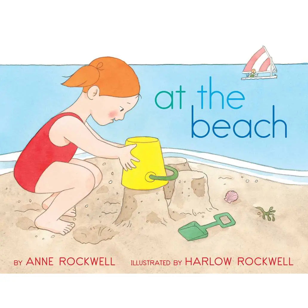 Book cover of 'At the Beach' with a child playing in the sand, a yellow bucket, and a green shovel.