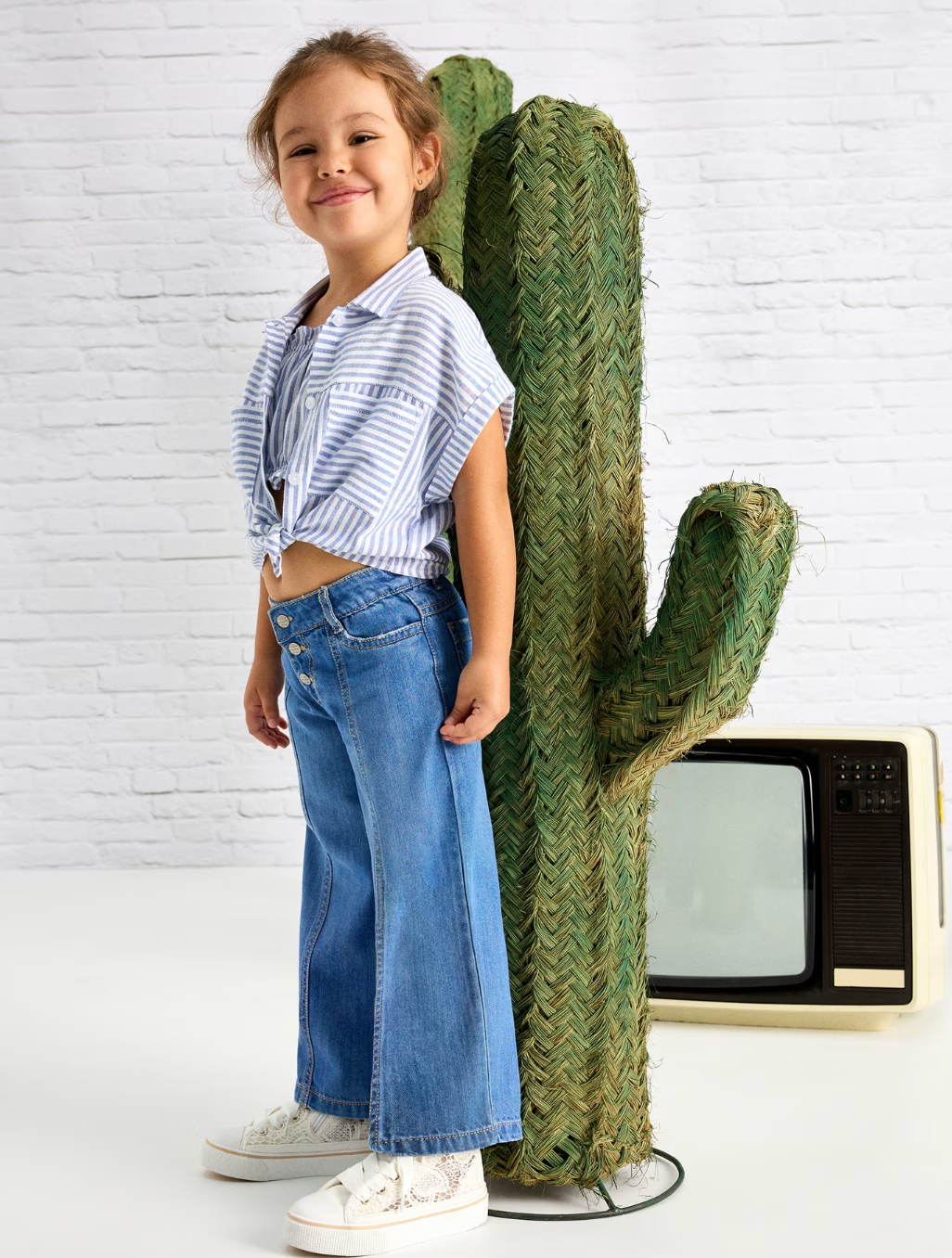 Little girl in wide leg jeans standing next to a cactus.