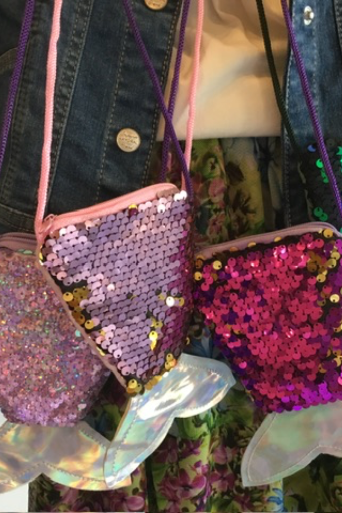 Three India Boutique sequin mermaid purses in pink and purple colors, displayed in front of a floral background.