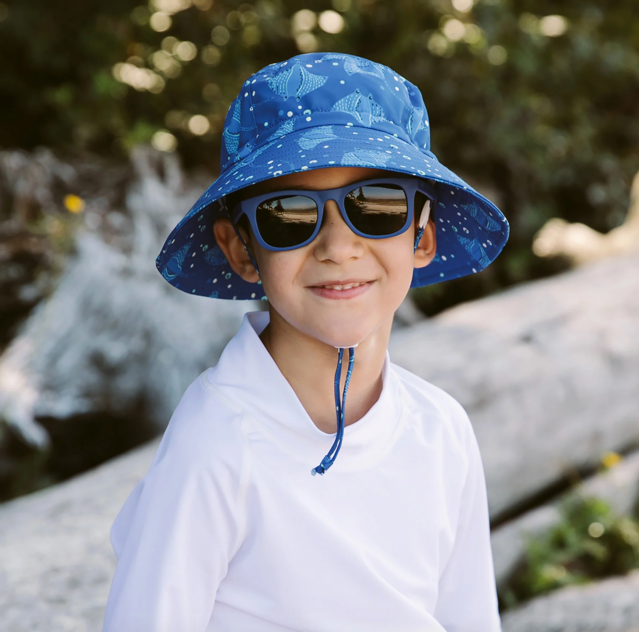 A boy wearing a Jan & Jul Manta ray printed bucket hat t the beach