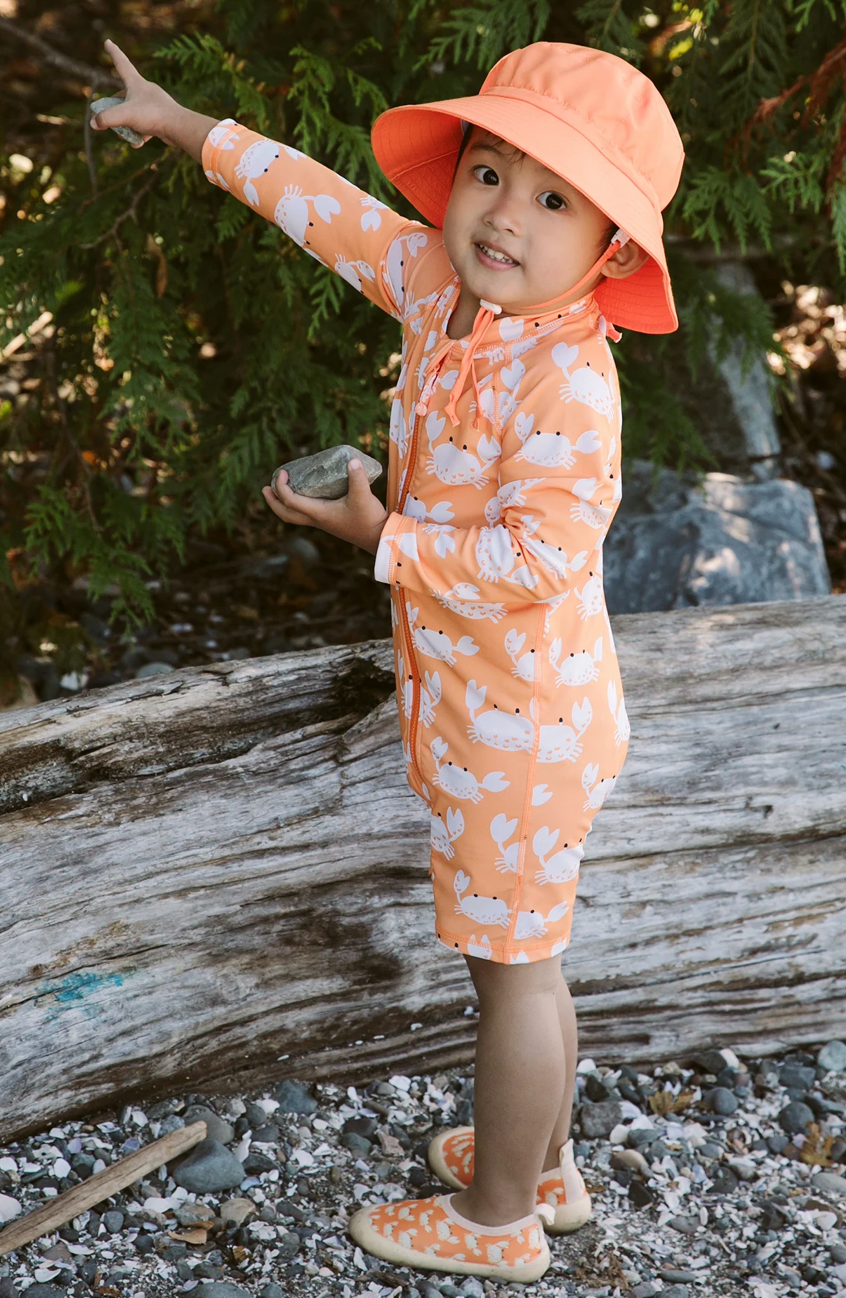 Little kid wearing Jan & Jul orange bucket pointing at the trees