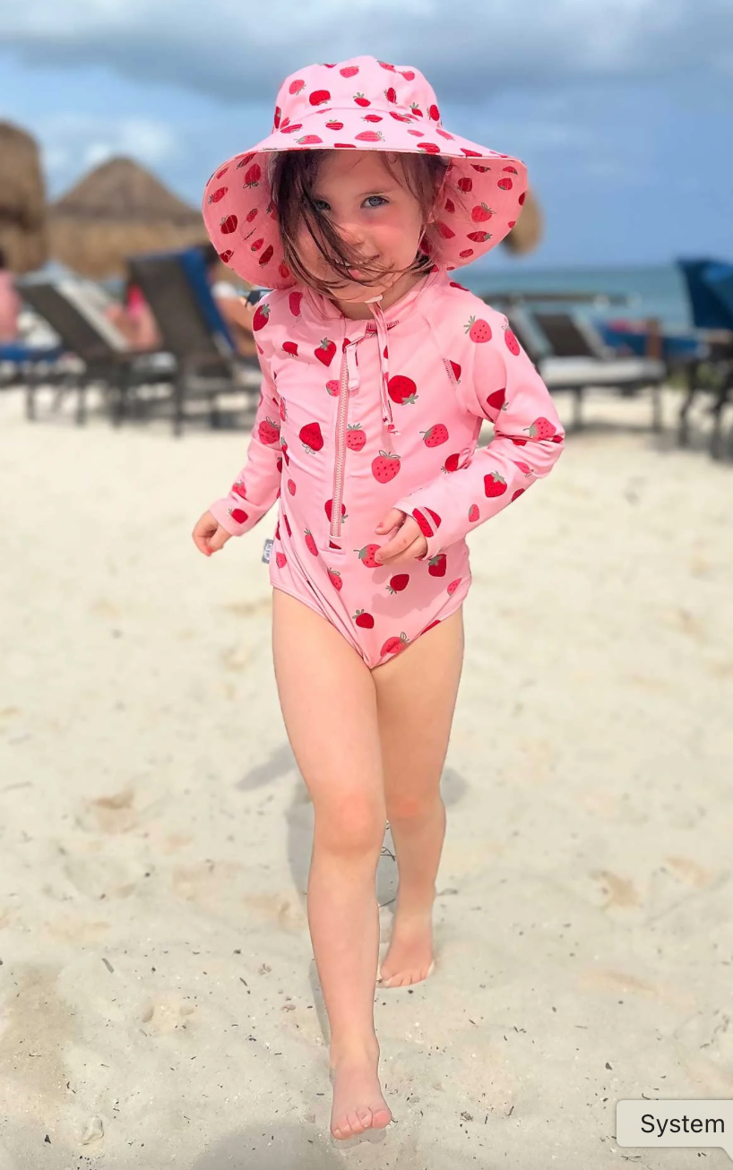 Girl on the beach wearing the Jan & Jul bucket hat with strawberries print