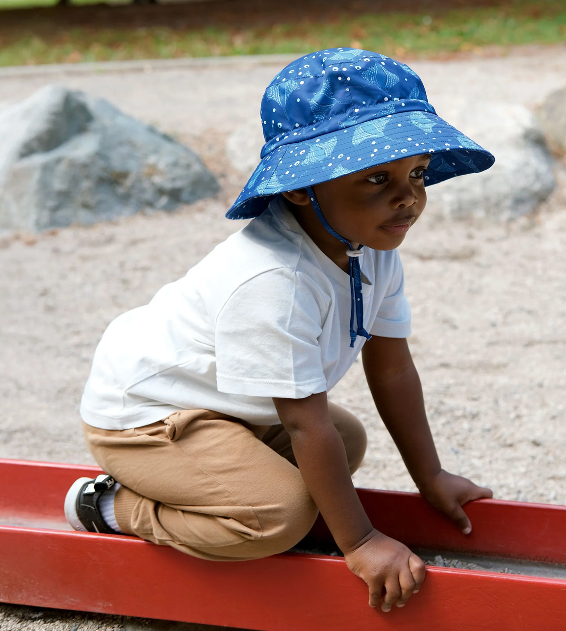 A little boy playing at the beach in a Jan & Jul bucket hat