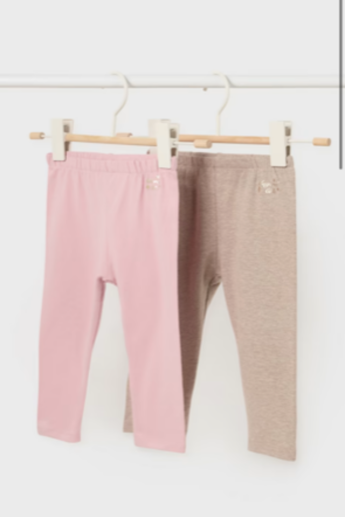 Two pairs of Mayoral baby leggings hanging on wooden hangers, one in soft pink and the other in light tan color.
