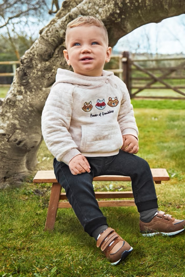 A baby wearing black Denim Joggers sitting on a wooden bench in a natural outdoor setting.