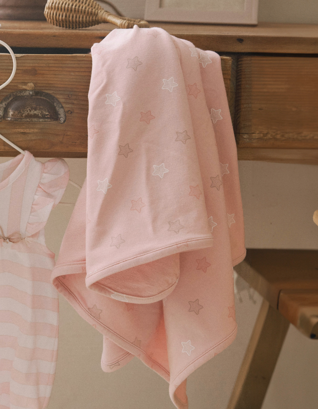 Pink Star Printed swaddle blanket hanging on a dresser drawer.