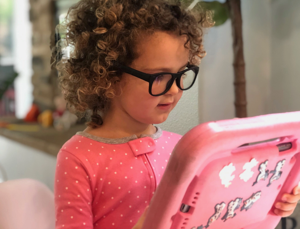 Child wearing blue light glasses and playing with a pink tablet