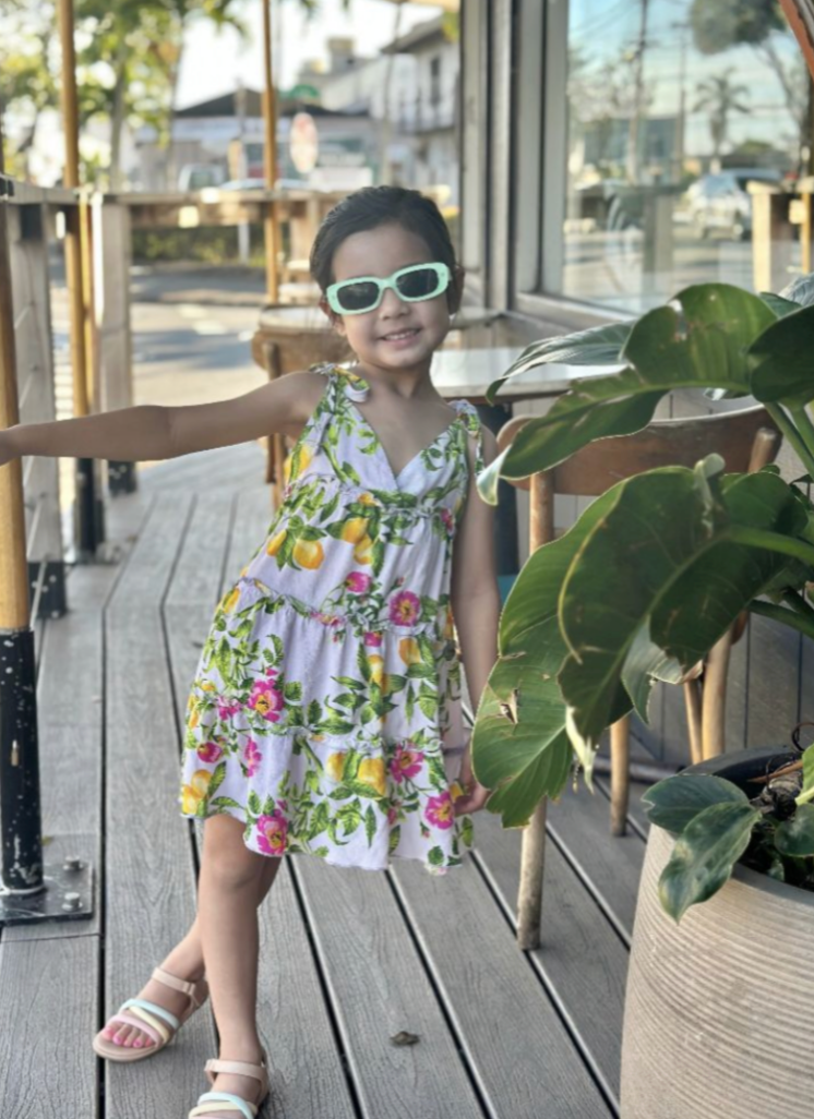 Child wearing a floral dress and sunglasses on a wooden deck.