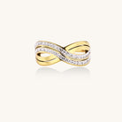Gold-plated stainless steel ring with crossed infinity bands adorned with sparkling rhinestones against cream background.