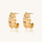 Close-up of dimensional gold-plated hoop earrings with rippled wave texture against white background.