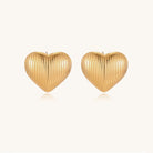 Close-up of ridged heart-shaped gold-plated stud earrings with textured surface pattern on cream background.
