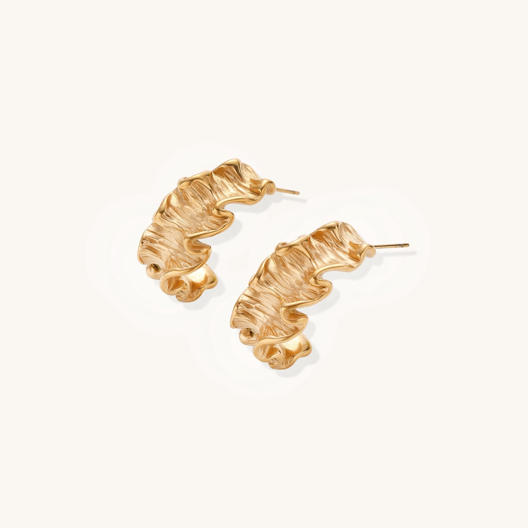 Textured gold-plated hoop earrings with wavy sculptural ridges displayed against a neutral background.