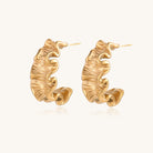 Textured gold-plated hoop earrings with wavy sculptural ridges displayed against a neutral background.