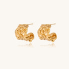 Textured gold-plated hoop earrings with organic molten surface pattern on cream background, showing intricate flowing details.