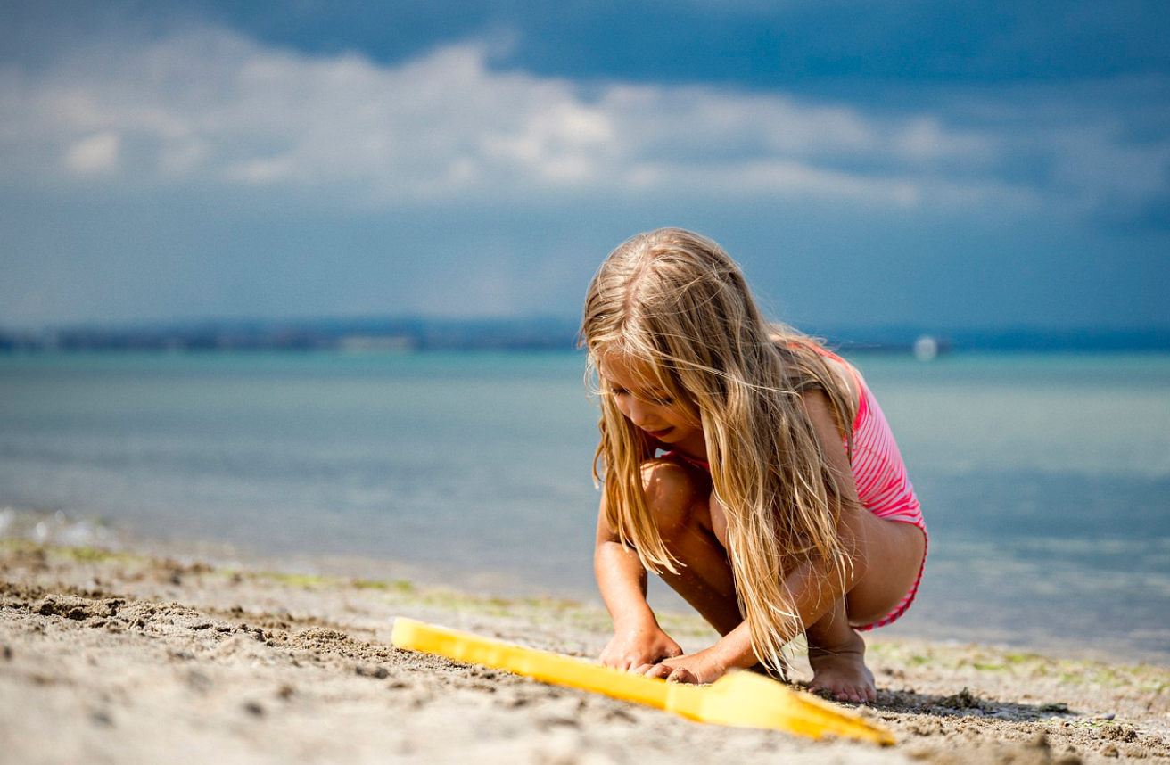 Blonde girl on the beach playing in the sand