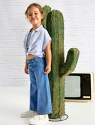 Little girl in wide leg jeans standing next to a cactus. 