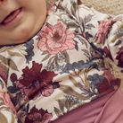 Close-up of a child wearing a Green Cotton Group floral-patterned outfit with pink and brown flowers.