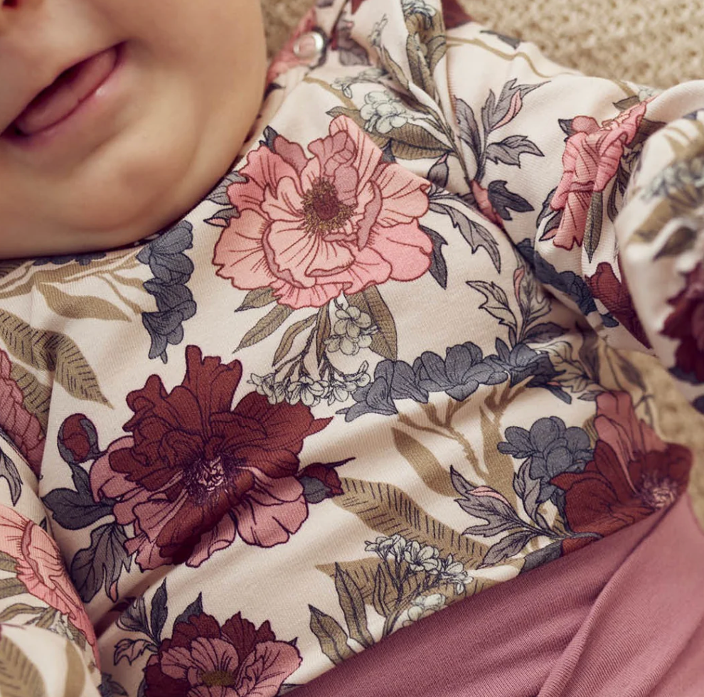 Close-up of a child wearing a Green Cotton Group floral-patterned outfit with pink and brown flowers.