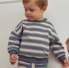 Child wearing a Green Cotton Group blue and white striped sweater against a plain background