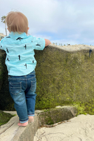 Little boy wearing Me & Henry Mark jeans on the beach leaning on a rock.