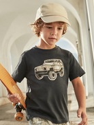 Boy wearing an off road t-shirt walking with a skateboard.