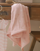 Pink Star Printed swaddle blanket hanging on a dresser drawer. 