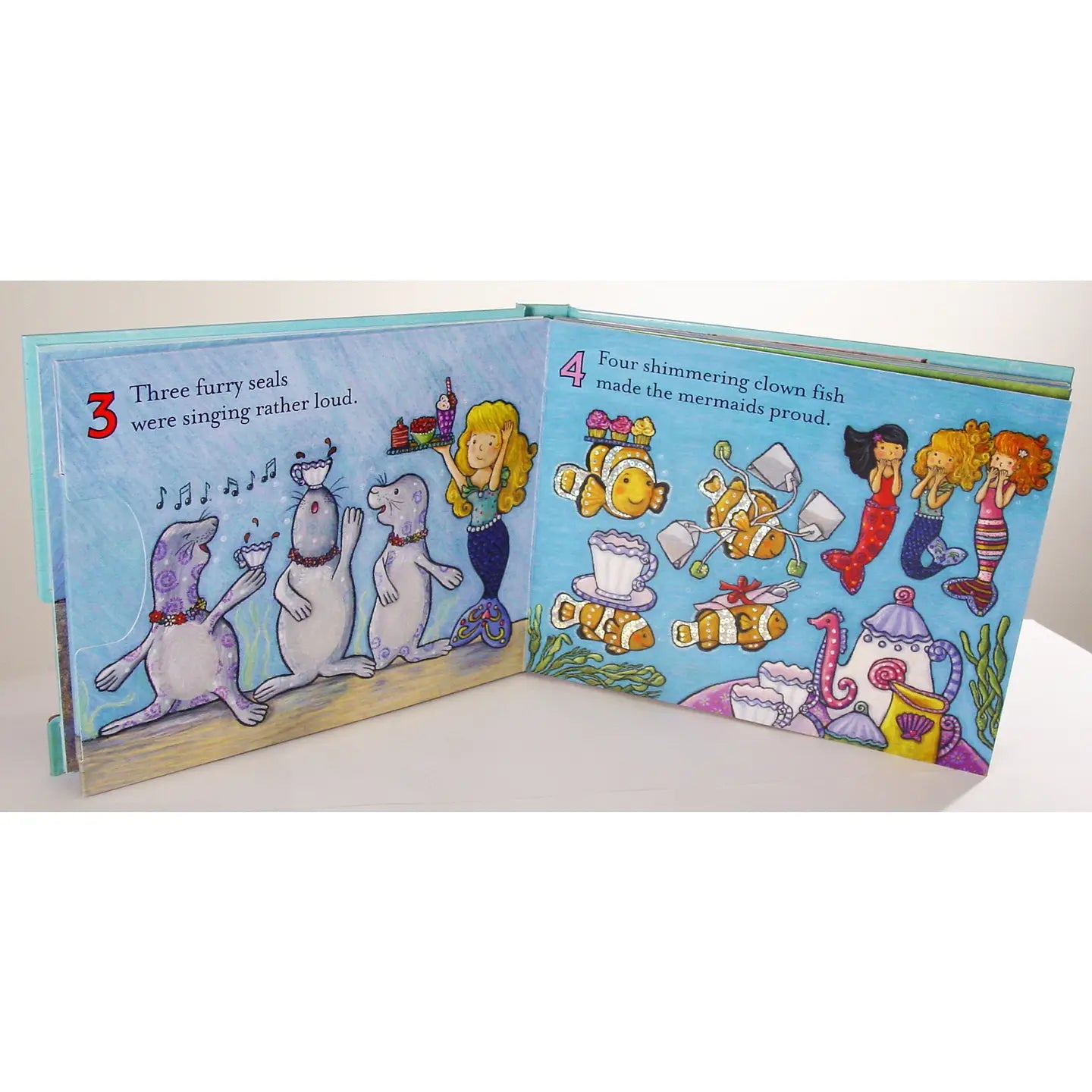 Open children's book with illustrations of seals, clownfish, and mermaids on a white background